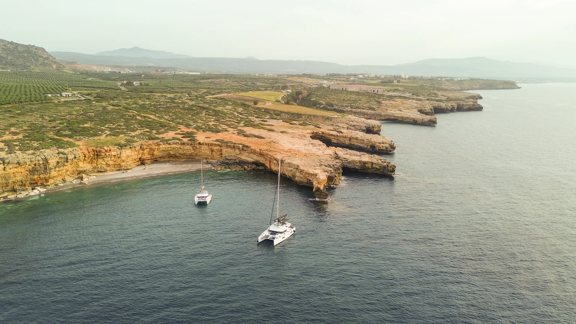 Catamarans anchored along a rocky Greek coastline