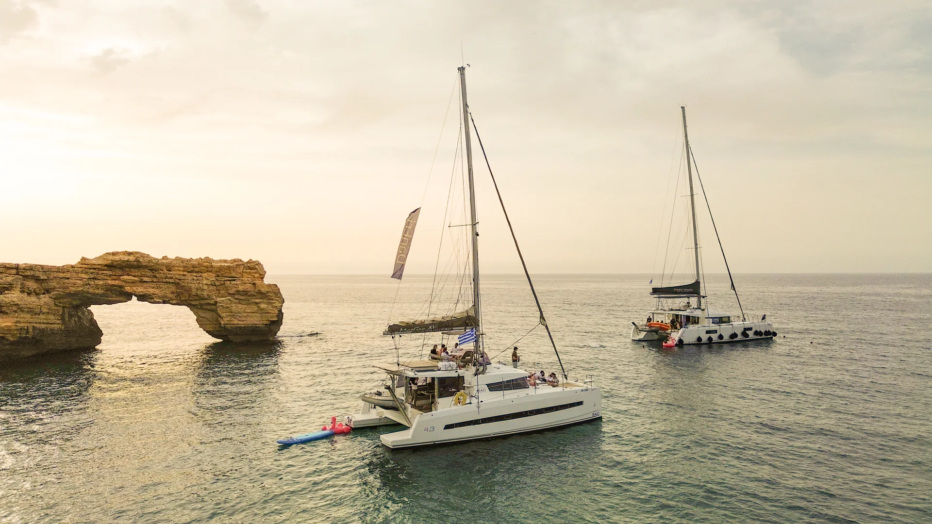 Catamarans near a coastal rock arch in the evening light
