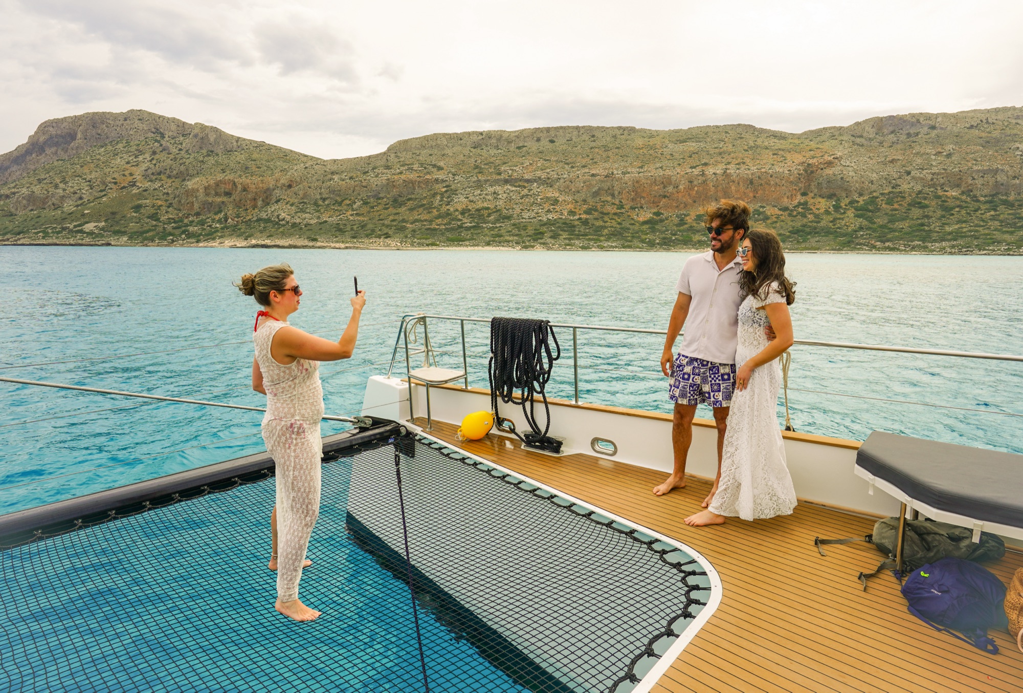 A couple on a DanEri catamaran's bow net over the turquoise water near Balos and Gramvousa