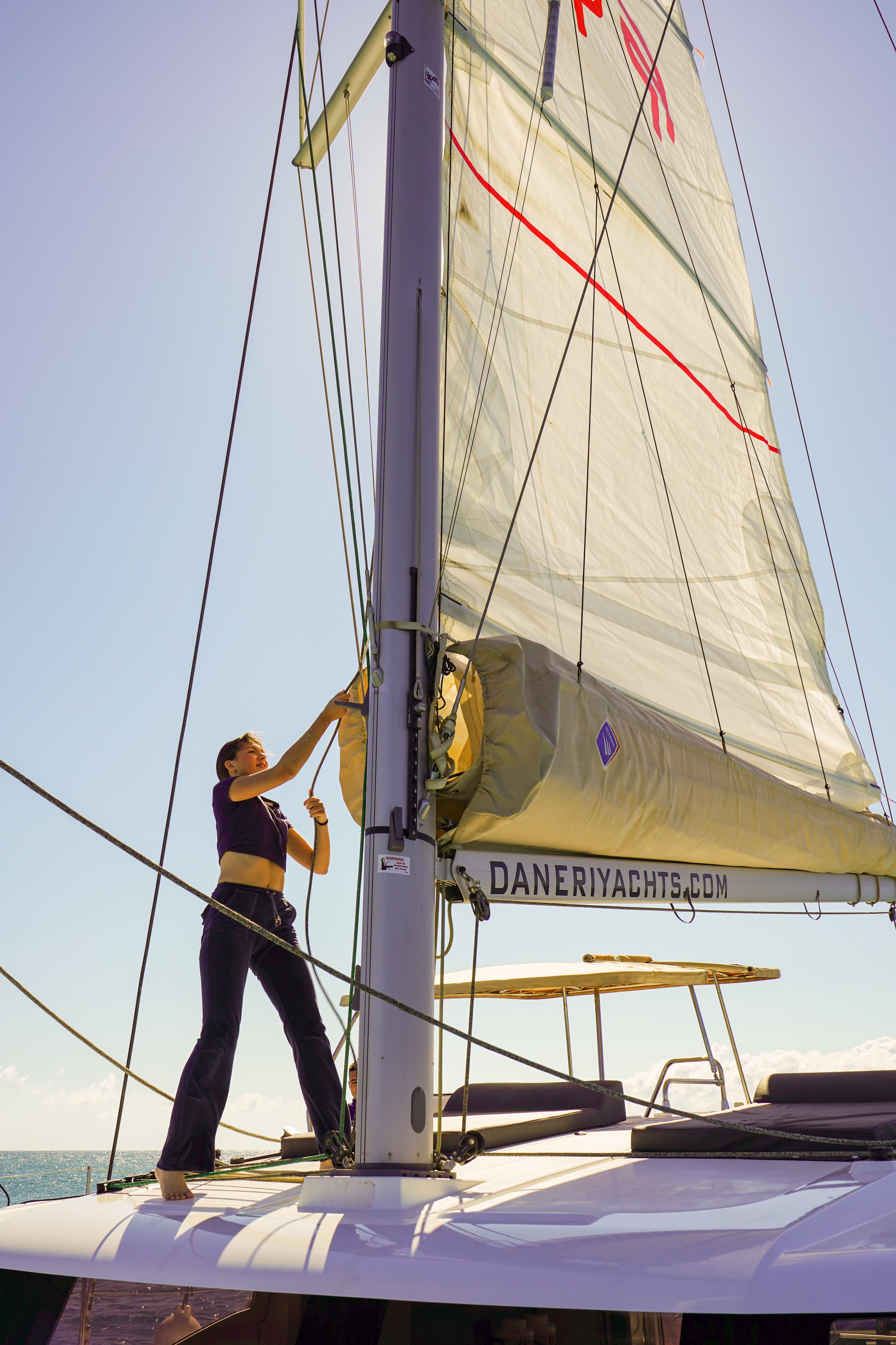 Raising the mainsail on a DanEri catamaran sailing off the coast of Crete